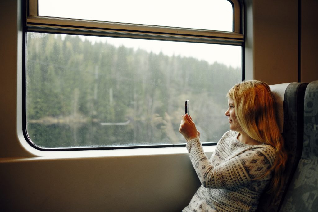 Kvinne sitter på tog og tar bilde av skogen hun ser ut vinduet