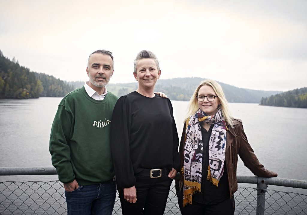 Tre personer, fra venstre: Barham Azadi, Åse Kristina Heien og Silje Louise Waters, som står oppstilt foran et stort vann. de tre lener seg på et rekkverk av metall.