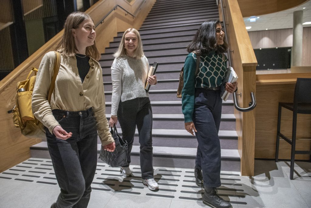 Tre unge kvinner med sekker og skolebøker går foran en trapp