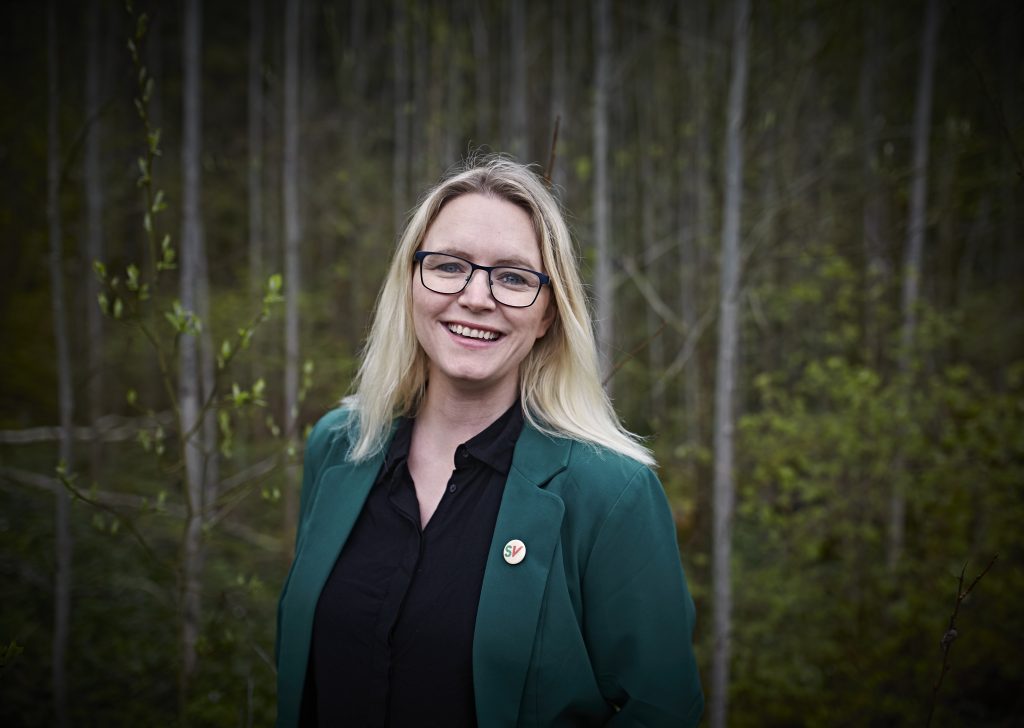Bilde i profil av Silje Louise Waters i sort skjorte med en mørkegrønn blazer. Silje smiler mot kamera, i med en mosegrodd skog i bakgrunnen.